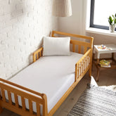 white bamboo toddler fitted sheet from the Signature Collection, viewed from above on a light wood frame toddler bed in a bright modern nursery