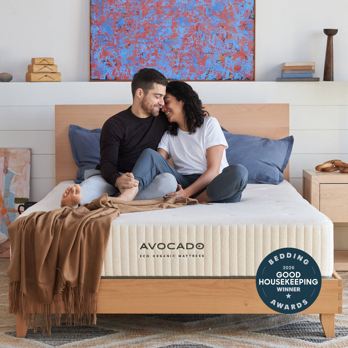 Couple sitting on a bed with an Avocado certified organic mattress, on an Avocado City Bed Frame.
