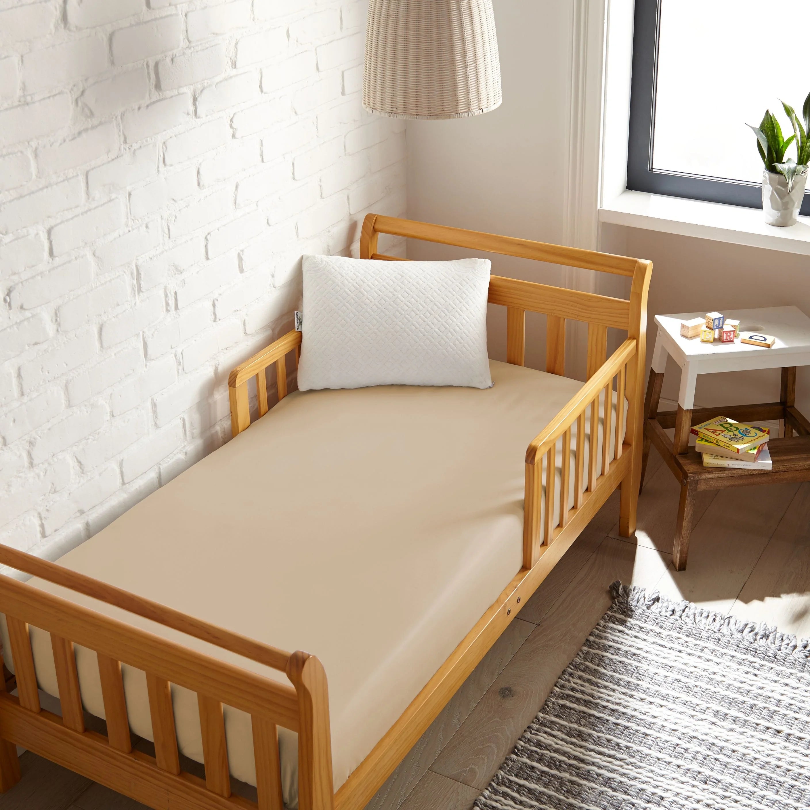 taupe bamboo toddler fitted sheet from the Signature Collection, viewed from above on a light wood frame toddler bed in a bright modern nursery